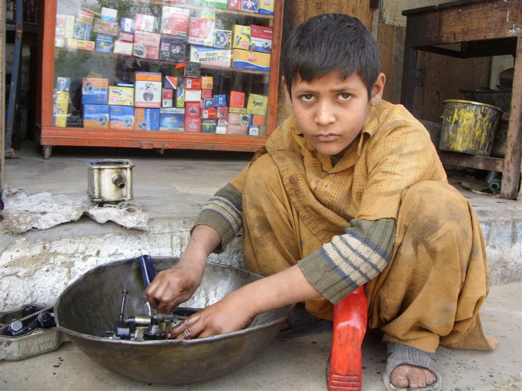 A young boy washing motorcycle parts instead of attending school due to financial hardship